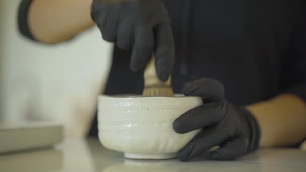 Close-up tangan dalam sarung tangan hitam mengaduk kopi dalam cangkir kecil. Tak dikenal profesional campuran barista kaukasia bahan untuk minuman panas di kafe. — Stok Video