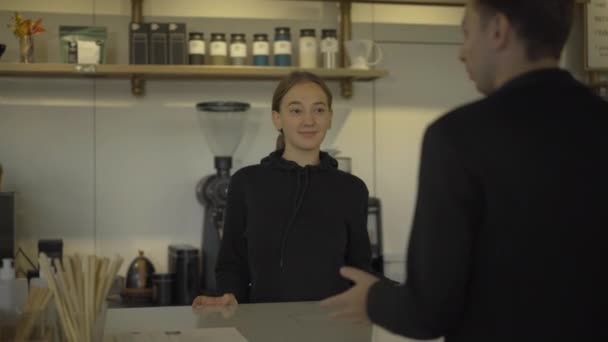 Portræt af positiv kaukasiske unge kvinde modtager ordre fra klienten i cafe og giver mand to kopper med kaffe-til-gå. Smilende bartender betjener kunden. – Stock-video