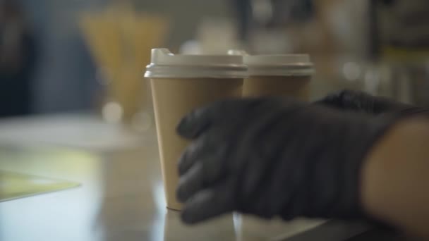 Zijaanzicht van barista handen die afhaalkoffie doorgeven aan de klant. Onherkenbare blanke vrouw in beschermende handschoenen die warme drank voor de man serveert. Coronavirus restaurant bedrijf. — Stockvideo