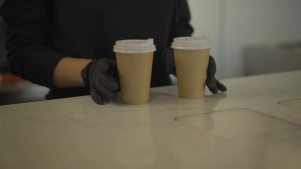 Onherkenbare barman in zwarte handschoenen die twee koffiekopjes aan een blanke man over de toonbank geeft. Barista serveert klant in café of restaurant. — Stockvideo