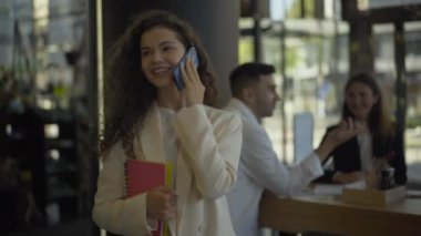 Gülümseyen genç bir kadın kafede yürüyor ve telefonda konuşuyor. Kahve molasına çıkan beyaz iş kadınının portresi. Öğle yemeğinde kendine güvenen bir CEO..