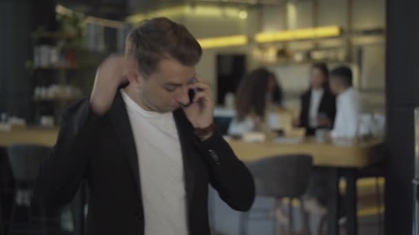 Retrato de un guapo y nervioso hombre de negocios caucásico hablando por teléfono con una cafetería borrosa al fondo. Empresario joven y estresado trabajando durante el almuerzo. — Vídeos de Stock