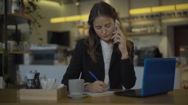 젊은 여성 CEO 가 카페에서 테이블에 앉아 전화로 통화를 하고 전화를 걸었습니다. 성공 한 백인 사업가가 쉬는 시간에 점심을 먹는 모습. 사업과 과로. — 비디오