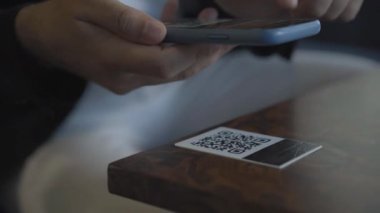 Tanımlanamayan beyaz adam akıllı telefonuyla QR kodunu tarıyor. Erkek eller telefonu tutuyor ve ekrandan dinliyor. Kafe veya restoranda modern menü.