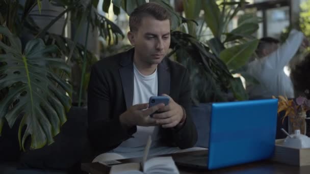 Homme d'affaires caucasien concentré utilisant smartphone et ordinateur portable dans le café. Portrait de jeune homme beau qui travaille en ligne pendant le déjeuner. Concept de réussite et mode de vie des entreprises. — Video