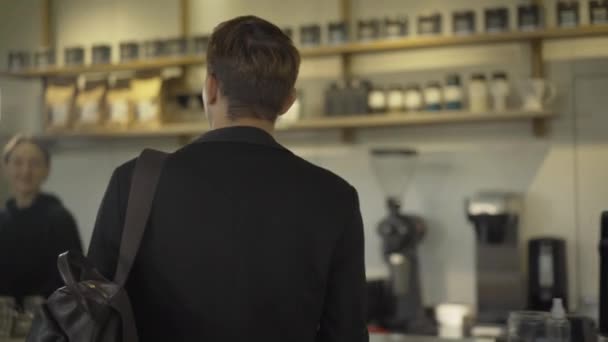 Camera volgt vertrouwen Kaukasische man lopen naar de toonbank in cafe. Achteraanzicht van brunette jonge zakenman met koffiepauze. Levensstijl van de ondernemer. — Stockvideo