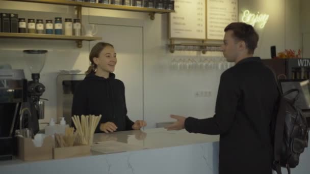 Morena hombre caucásico tomando tazas de café para llevar de la mujer sonriente en la cafetería y salir. Una barista positiva sirviendo a un cliente masculino en el restaurante. Concepto de ruptura empresarial. — Vídeos de Stock