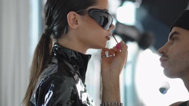 Şık bir makyaj sanatçısı şık, modern stüdyo ortamındaki bir modele titizlikle canlı bir dudak rengi sürüyor.