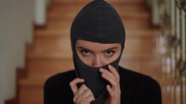 Siyah elbiseli sarışın bir kız, soygundan sonra maskesini çıkarıp, evdeki ahşap merdivenlerde otururken saçlarını özgürce sallıyor..