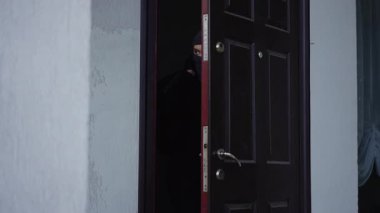 Maskeli bir şahıs, elinde bir çantayla gizlice bir eve girer ve güvenlik farkındalığı temasını vurgular..