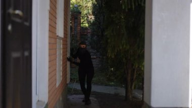 Gölgeli bir figür sinsice ve ihtiyatlı bir şekilde uğursuz görünen bir binaya doğru hareket eder. Gerginliği ve belirsizliği artırır.