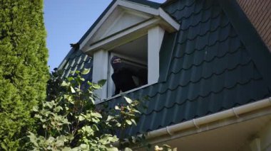 Siyah elbiseli ve maskeli bir kız tavan arası penceresinden sarkmış, bir sonraki hamlesini yapmadan önce evin etrafını dikkatlice izliyor..