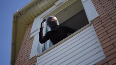 Karanlık bir pencereye kaygı verici bir şekilde bakan maskeli bir figür, bu gergin anın entrika ve gerilimini artırıyor.