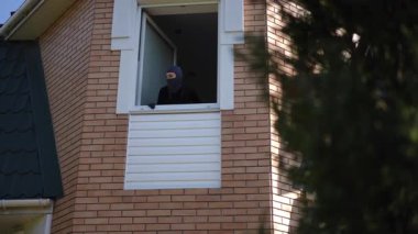 Siyah maske takan kız hırsızlar açık pencereden dürbünle etrafı dikkatle izler ve kaçmadan önce tehlikeyi kontrol eder..