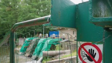 Üzerinde el işareti olan kırmızı ve beyaz uyarı işareti hidroelektrik santralinin yakınındaki yeşil çite iliştirilmiştir. Bu da güvenlik erişiminin kısıtlı olduğunu gösterir..