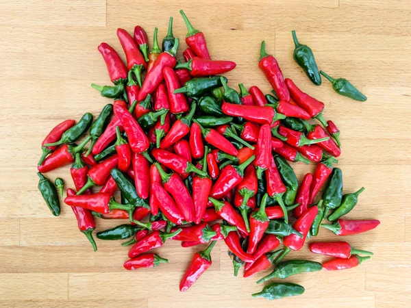 Piros és zöld chili paprika. Halom fa munkalap. — Stock Fotó
