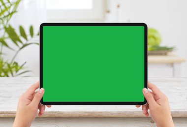 İzole edilmiş iki el, siyah tablet medya aygıtı, beyaz ekran maketi ve ahşap masa.