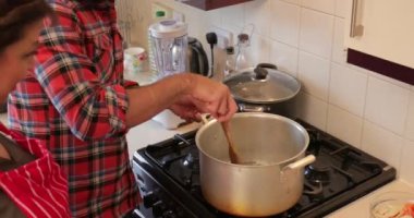 Yetişkin adam akşam yemeği yapmak için annesi yardım ediyor. O bir köri soba üzerinde büyük bir tencerede karıştırarak. 