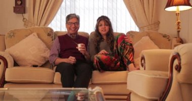 Olgun çift televizyon izlerken bir yoğurt paylaşımı evlerinin oturma odasında rahatlatıcı.