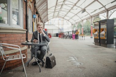 İşe gitmek için genç işadamı trainstation beklemek süre, kahve içme.