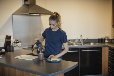 Onun yumurtalı sandviç ile kahvaltıda çay bir fincan için bir bardağa bir genç kadın yetişkin sıcak su dökerek önden görünümü.