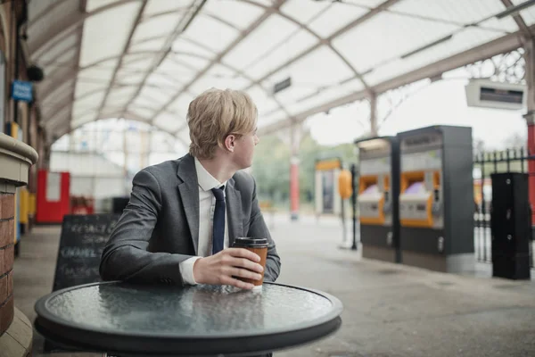 一杯のコーヒーと Trainstatio で待っているビジネスマン 回すと列車時刻表を見て — ストック写真