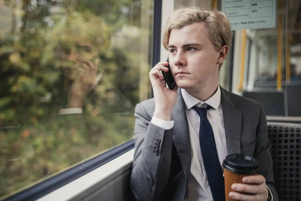 Businessman on the phone with a cup of coffee on the train during his commute to work.