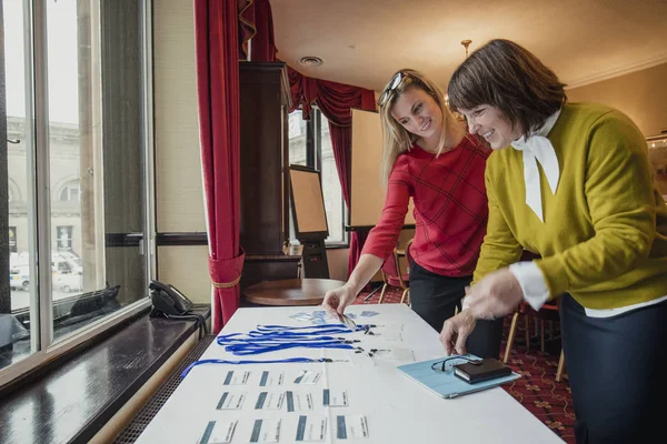 Two businesswomen looking for their name badges on the table before the conference starts.