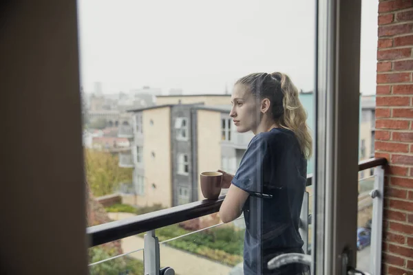 バルコニーでお茶を楽しんで彼女のカジュアルな服装の若い女性大人のウィンドウ ビューを使用 — ストック写真