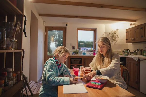 Mother and daughter sitting at the table in the morning. Mother is helping her daughter with her homework before school.