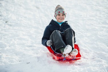O karda bir kızak üzerinde bir tepeden aşağı gelir olarak küçük çocuk kamera için gülümsüyor.