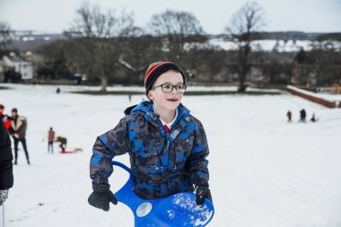 Küçük çocuk geri büyük bir tepe aşağı karda kızakla sonra yürüyor.
