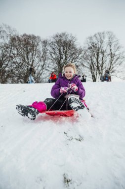 Küçük bir kızın karda bir tepeden aşağı kızakla düşük açılı görünüş.