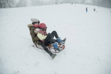 Two girls are holding on to each other as they go down a hill together on a sleigh. clipart