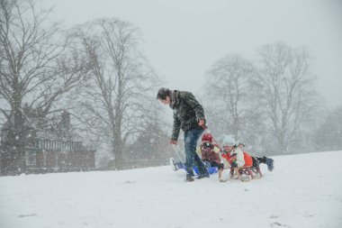 Man is pulling his children along in the snow on sleds.  clipart