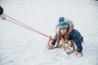 Küçük kız karda bir atlı kızak üzerinde çekti ise kamera için gülümsüyor.