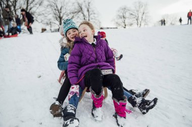 Üç küçük kız bir kızağa birlikte, karda bir tepeden aşağı gidiş oturuyorsun. 