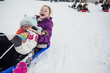 Çocuk toplumun genel bir parkta büyük bir tepe üzerinde karda bir kızak yarışı yaşıyorsanız.