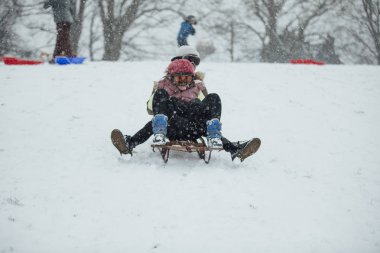 İki küçük kız birlikte karda bir kızak üzerinde büyük bir tepeden aşağı gidiyor. 