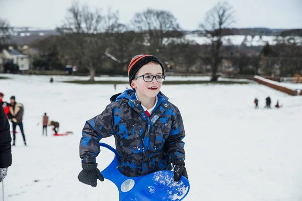 Küçük çocuk geri büyük bir tepe aşağı karda kızakla sonra yürüyor.