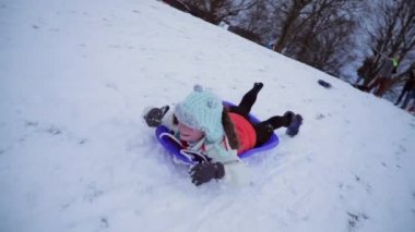 Küçük kız karnı bir kızak üzerinde karda bir tepeden aşağı gidiş yatıyor.