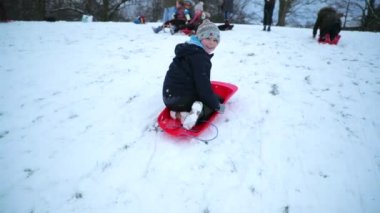 Küçük çocuk bir tepeden aşağı ters karda bir kızak üzerinde kayıyor.