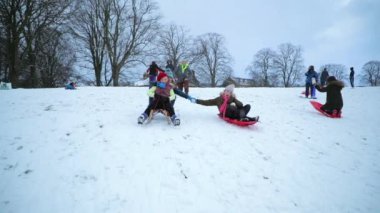 Küçük kızlar bir tepeden aşağı karda kızaklarımız üzerinde itilir.