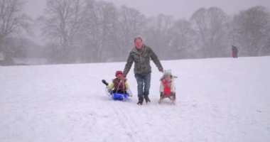 Olgun adam karda bir kızak üzerinde onun kızı çekiyor.