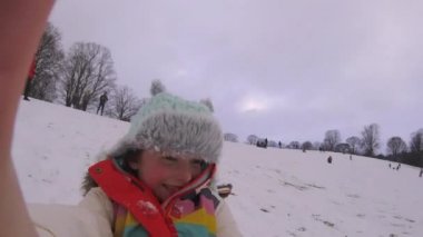 Küçük kız bir selfie o karda bir tepeden aşağı kızaklarımız bir eylem cam kullanarak video alıyor.