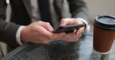 Görünümü, yakın çekim, bir paket kahve fincanı ile otururken akıllı telefonunu yazarak bir adamın arka.