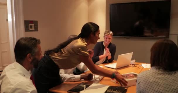 Vue arrière d'un groupe d'hommes et de femmes d'affaires qui travaillent tard. Une femme d'affaires apporte un plateau de beignets .