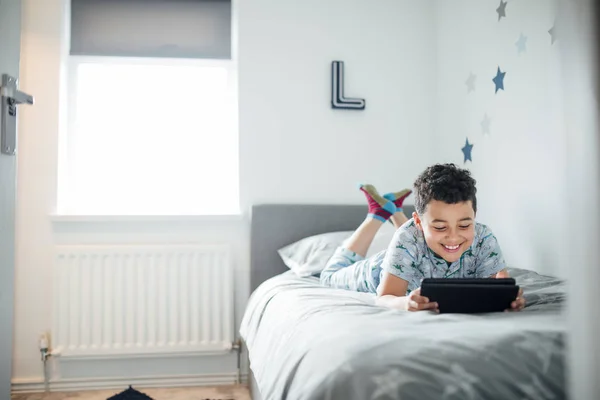 Menino Está Deitado Sua Cama Manhã Usando Tablet Digital — Fotografia de Stock