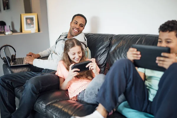 Siblings Playing Together Handheld Consoles Sofa Home While Father Using — Stock Photo, Image