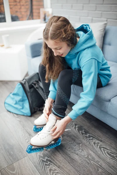 Little girl is putting figure skates on in the conservatory of her home before she goes to her skating lesson.
